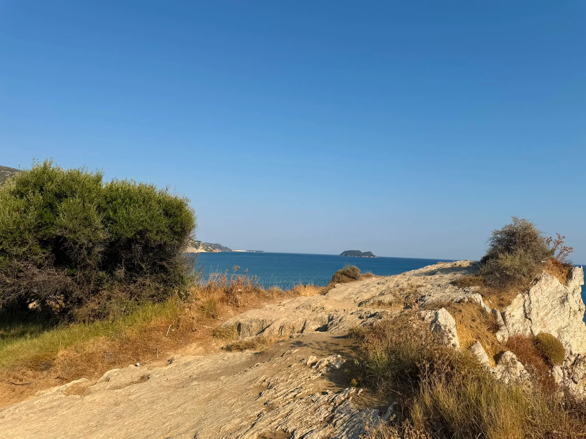 The clifftop path down to the beach, with the sea and a small offshore islet on the horizon