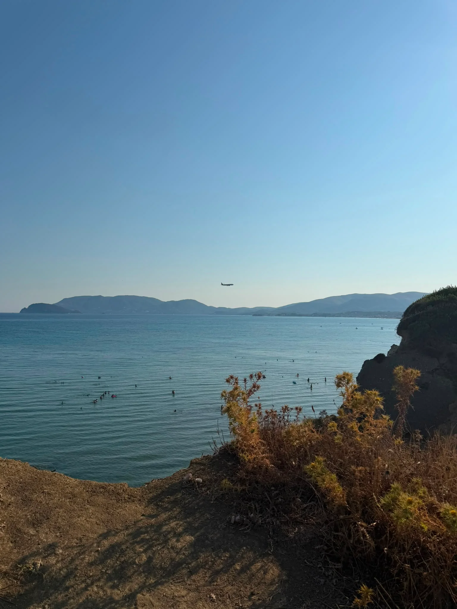 Swimmers in the calm, shallow water off Crystal Beach, with the mountains of Laganas Bay beyond