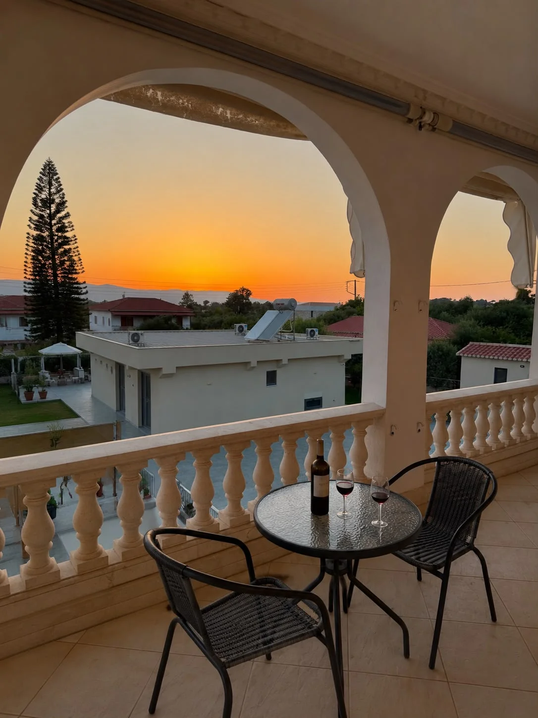 A glass-top table set with wine glasses on the balcony, framed by the archways as the sun sets
